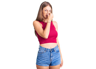 Fototapeta premium Young beautiful blonde woman wearing elegant summer shirt smelling something stinky and disgusting, intolerable smell, holding breath with fingers on nose. bad smell