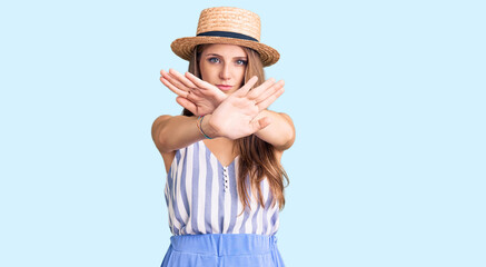 Obraz na płótnie Canvas Young beautiful blonde woman wearing summer hat rejection expression crossing arms and palms doing negative sign, angry face