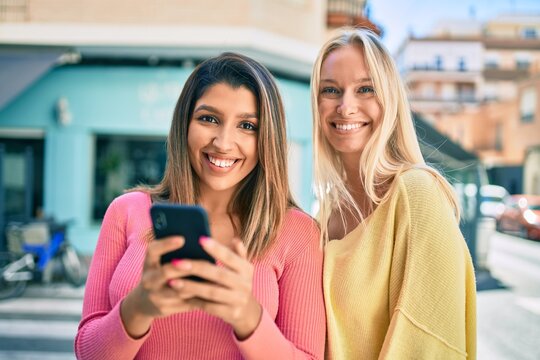 Two beautiful and young girl friends together having fun at the city using smartphone