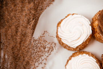 Small sweet tartlets with brown cream in a white plate next to pampas grass	