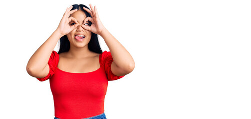Fototapeta premium Young beautiful asian girl wearing casual clothes doing ok gesture like binoculars sticking tongue out, eyes looking through fingers. crazy expression.
