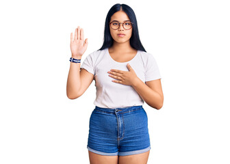 Obraz premium Young beautiful asian girl wearing casual clothes and glasses swearing with hand on chest and open palm, making a loyalty promise oath