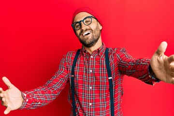 Handsome man with beard wearing hipster elegant look looking at the camera smiling with open arms for hug. cheerful expression embracing happiness.