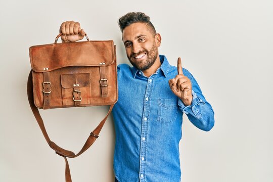 Handsome man with beard holding business bag smiling with an idea or question pointing finger with happy face, number one