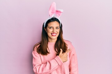 Beautiful hispanic woman wearing cute easter bunny ears smiling cheerful pointing with hand and finger up to the side