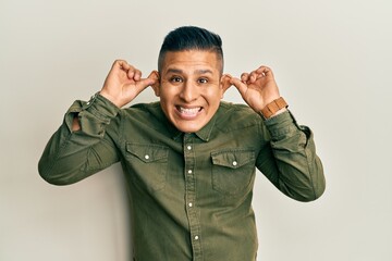 Young latin man wearing casual clothes smiling pulling ears with fingers, funny gesture. audition...