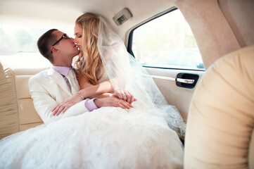 Young newlyweds in car at the wedding. The groom hugs the bride.