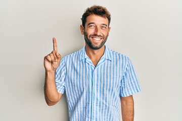 Handsome man with beard wearing casual shirt smiling with an idea or question pointing finger up with happy face, number one