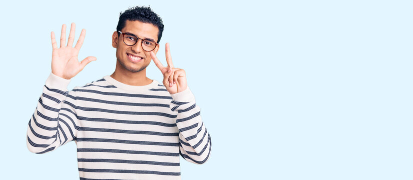 Hispanic handsome young man wearing casual clothes and glasses showing and pointing up with fingers number seven while smiling confident and happy.