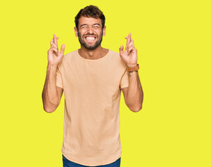 Handsome young man with beard wearing casual tshirt gesturing finger crossed smiling with hope and eyes closed. luck and superstitious concept.