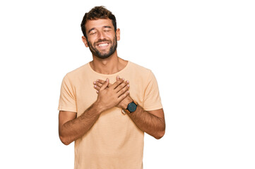 Handsome young man with beard wearing casual tshirt smiling with hands on chest with closed eyes and grateful gesture on face. health concept.