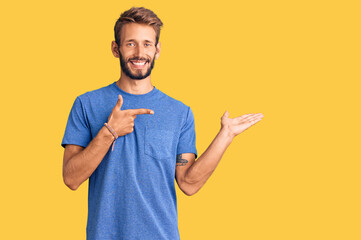 Handsome blond man with beard wearing casual clothes amazed and smiling to the camera while presenting with hand and pointing with finger.