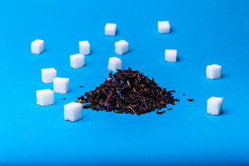 Heap of black tea and cubes of white sugar on a blue background.