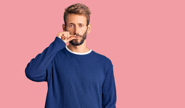 Handsome blond man with beard wearing casual sweater mouth and lips shut as zip with fingers. secret and silent, taboo talking