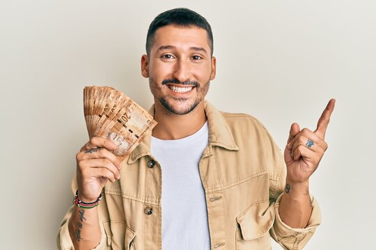 Handsome man with tattoos holding south african 20 rand banknotes smiling happy pointing with hand and finger to the side