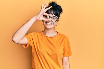 Young hispanic girl wearing casual clothes and glasses smiling happy doing ok sign with hand on eye looking through fingers