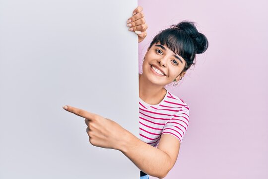Young hispanic girl holding blank empty banner smiling happy pointing with hand and finger