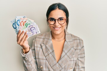 Young brunette woman holding singapore dollars banknotes looking positive and happy standing and smiling with a confident smile showing teeth