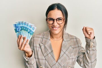 Young brunette woman holding hong kong 20 dollars banknotes screaming proud, celebrating victory and success very excited with raised arm