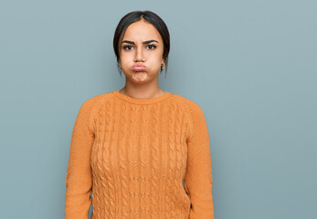 Young brunette woman wearing casual winter sweater puffing cheeks with funny face. mouth inflated...