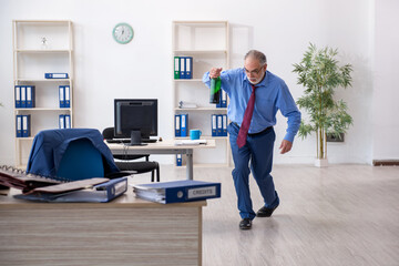 Old male employee drinking alcohol in the office