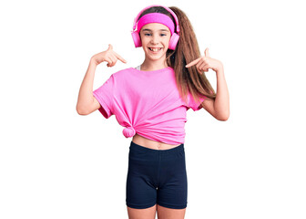 Obraz na płótnie Canvas Cute hispanic child girl wearing gym clothes and using headphones looking confident with smile on face, pointing oneself with fingers proud and happy.