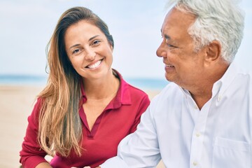 Middle age hispanic couple smiling happy sitting on bench at the beach.