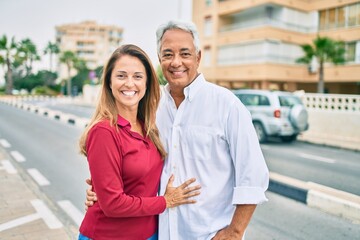 Middle age hispanic couple smiling happy and hugging walking at street.