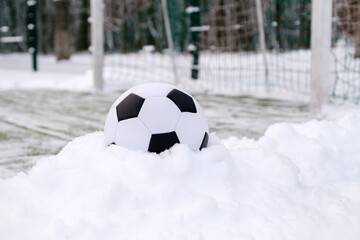 Soccer ball placed on snowdrift near goal in winter on sports ground