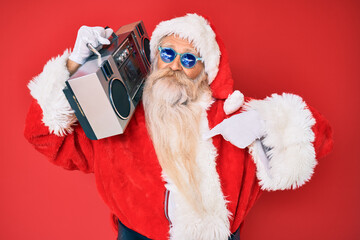 Old senior man wearing santa claus costume and boombox pointing finger to one self smiling happy and proud