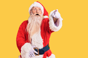 Old senior man with grey hair and long beard wearing traditional santa claus costume pointing with finger surprised ahead, open mouth amazed expression, something on the front