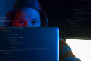 anonymous programmer, hacker in hoodie coding on laptop in dark room in red blue neon light, front...