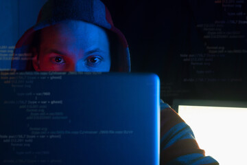 anonymous programmer, hacker in hoodie coding on laptop in dark room in red blue neon light, front view hacker gaze into  monitor and program code in screen, cyber security and hacking attack concept