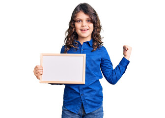 Fototapeta premium Cute hispanic child with long hair holding empty white chalkboard screaming proud, celebrating victory and success very excited with raised arms