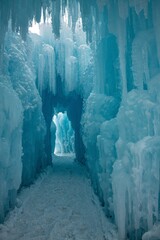 A walkway through ice. Blue and white icicles are hanging from above and the pathway is covered in snow.