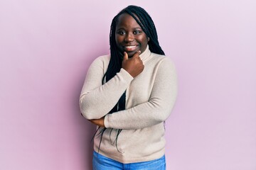 Young black woman with braids wearing casual winter sweater looking confident at the camera smiling with crossed arms and hand raised on chin. thinking positive.