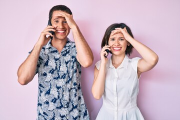 Beautiful couple having conversation talking on the smartphone stressed and frustrated with hand on head, surprised and angry face