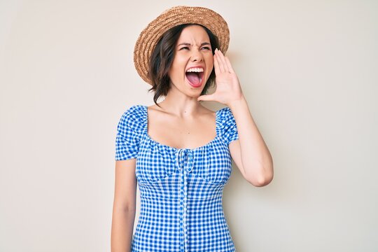 Young beautiful girl wearing summer hat shouting and screaming loud to side with hand on mouth. communication concept.