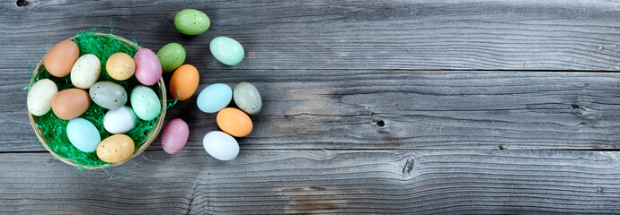 Happy Easter holiday concept with left border of basket of over flowing eggs and green grass on rustic wooden planks