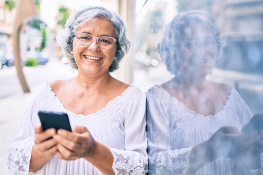 Middle age woman with grey hair smiling happy outdoors using smartphone