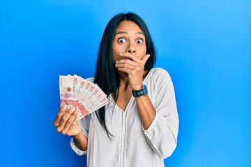 Young african american woman holding 10 colombian pesos banknotes shocked covering mouth with hands for mistake. secret concept.