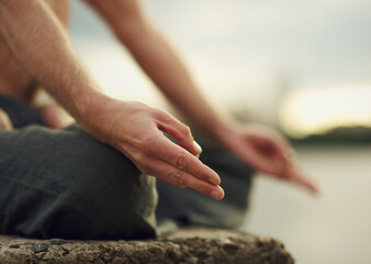 Shot focused on hands of a man doing yoga exercise on the shore