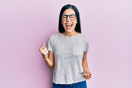 Beautiful young woman wearing casual clothes and glasses celebrating surprised and amazed for success with arms raised and eyes closed