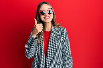 Young brunette woman wearing fashion and modern look doing happy thumbs up gesture with hand. approving expression looking at the camera showing success.