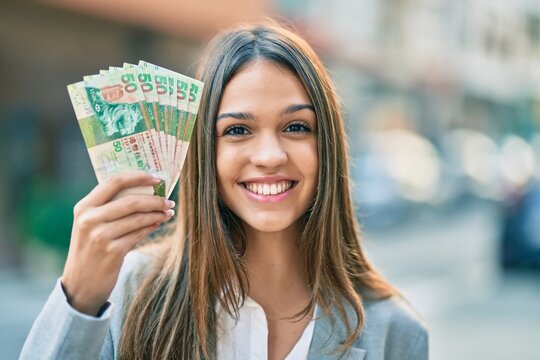 Young latin businesswoman smiling happy holding hong kong dollars at the city.