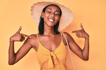 Young african american woman wearing summer hat looking confident with smile on face, pointing oneself with fingers proud and happy.