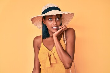 Young african american woman wearing summer hat looking stressed and nervous with hands on mouth biting nails. anxiety problem.