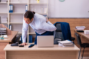 Young male employee suffering from backpain at workplace