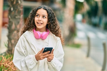 Beautiful hispanic girl smiling happy using smartphone and headphones at the city.