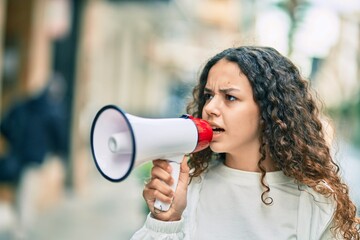 Hispanic child girl shouting angry using megaphone at the city.